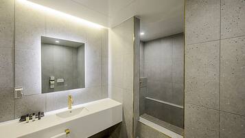 Un baño moderno con tocador blanco, un espejo grande y una zona de ducha.