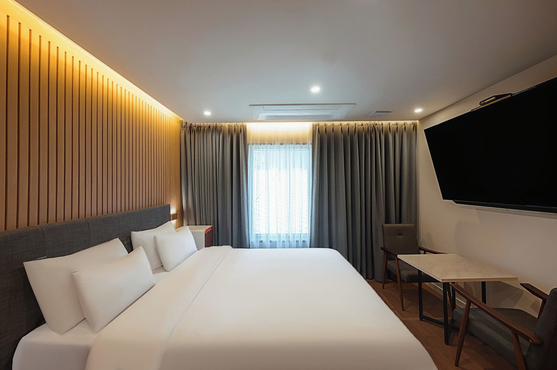 A hotel room with a large bed, a desk, a chair, a TV, and a window with curtains.