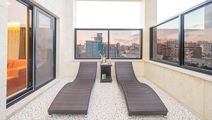 Un balcón con dos sillones de mimbre, una mesita con una botella y aperitivos, y vistas a la ciudad a través de amplios ventanales.