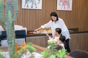 Una persona sirve comida a un niño en un mostrador con paneles de madera y una planta al frente.