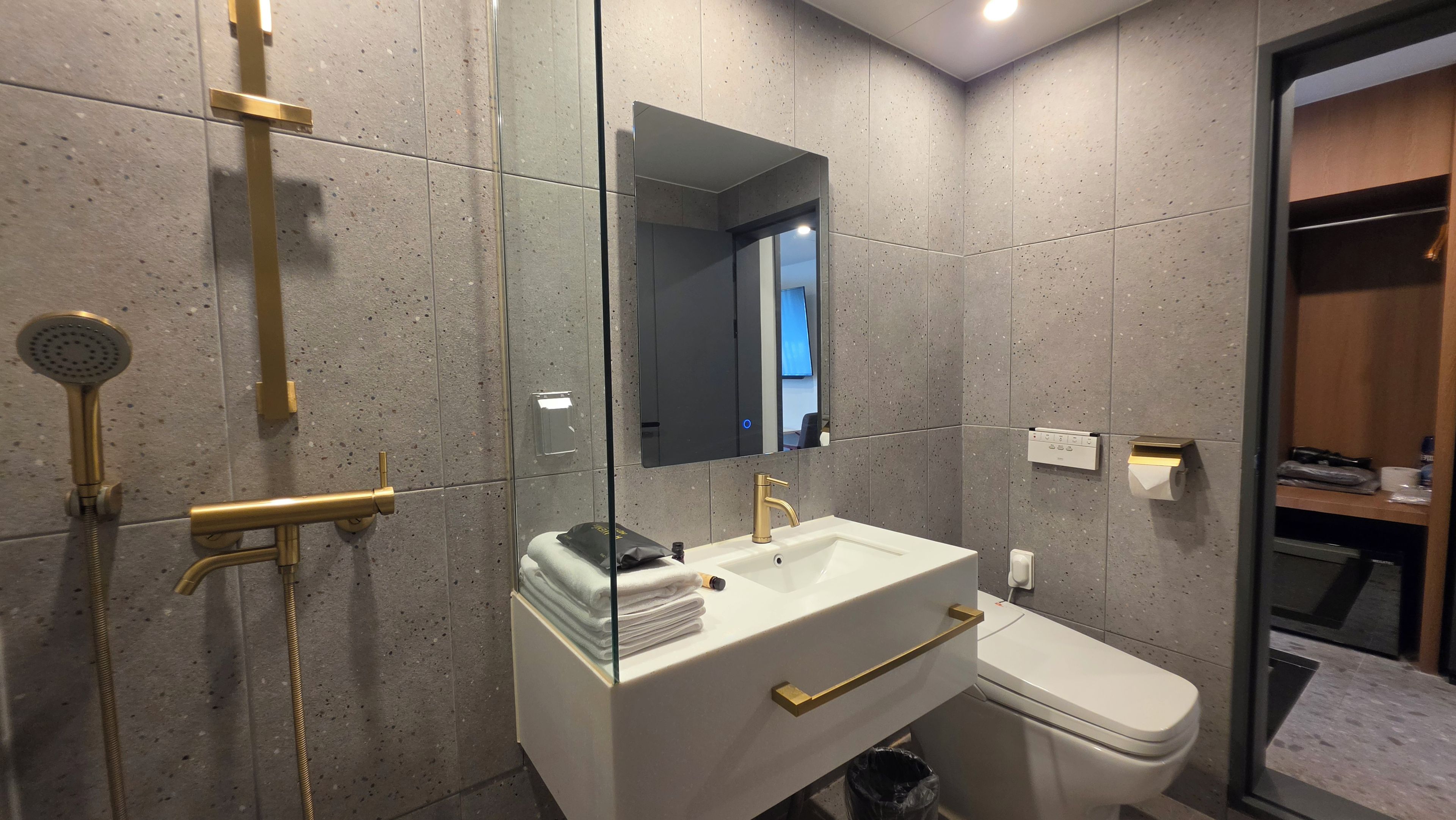 A modern bathroom with a glass shower enclosure, a white sink with gold fixtures, and a toilet.