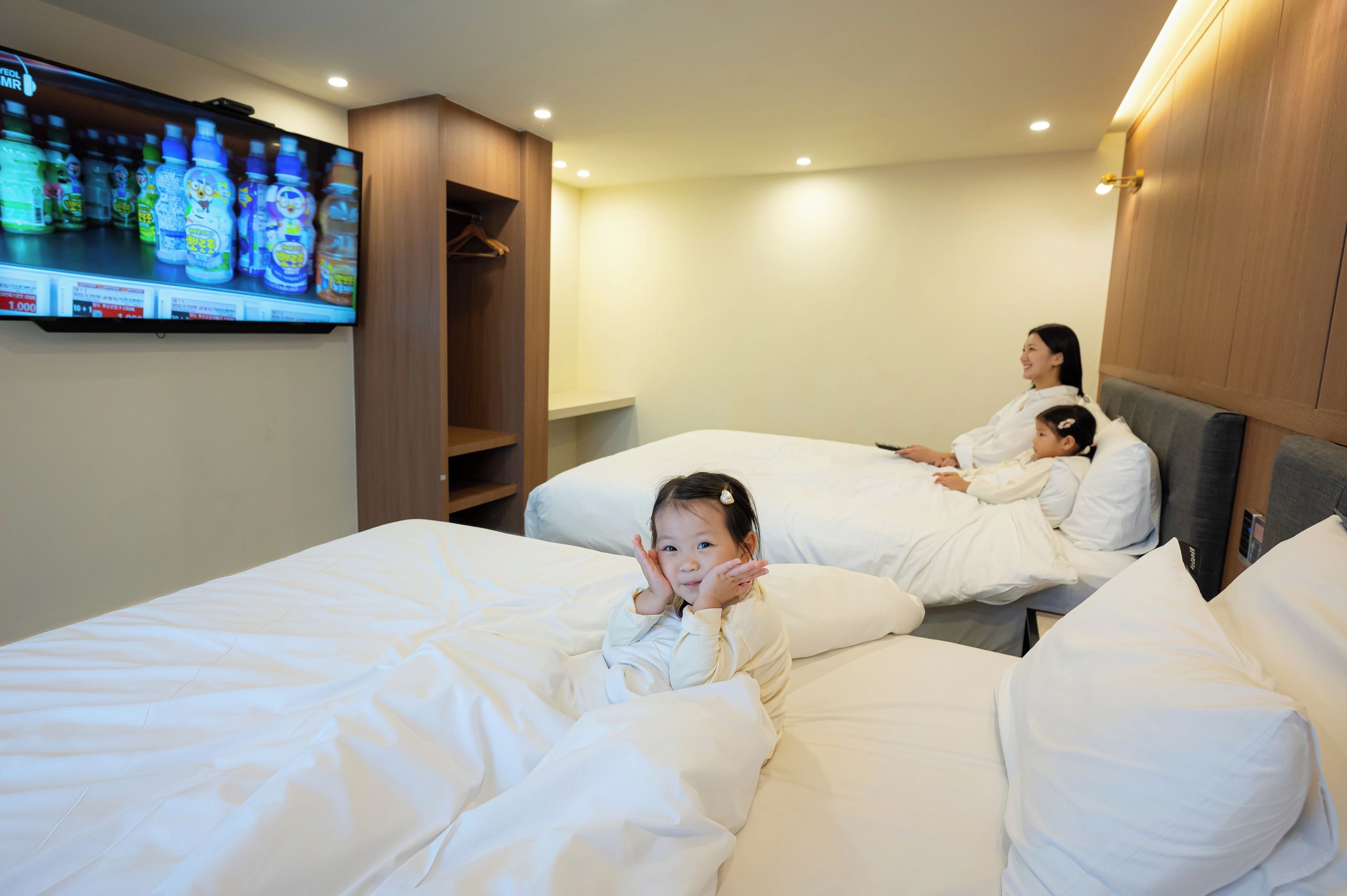A hotel room with two beds, a television on the wall, and a wooden wardrobe.