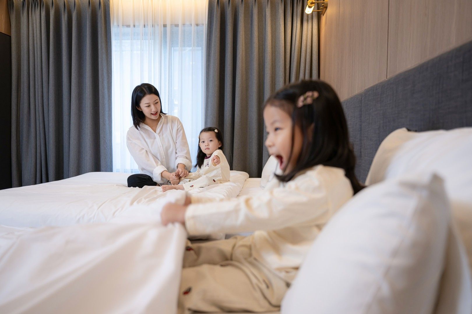 A hotel room with a bed, curtains, and a wall-mounted light fixture.