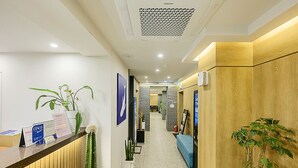 Zona de recepción de hotel con mostrador, plantas y una escalera que sube a los pisos superiores.