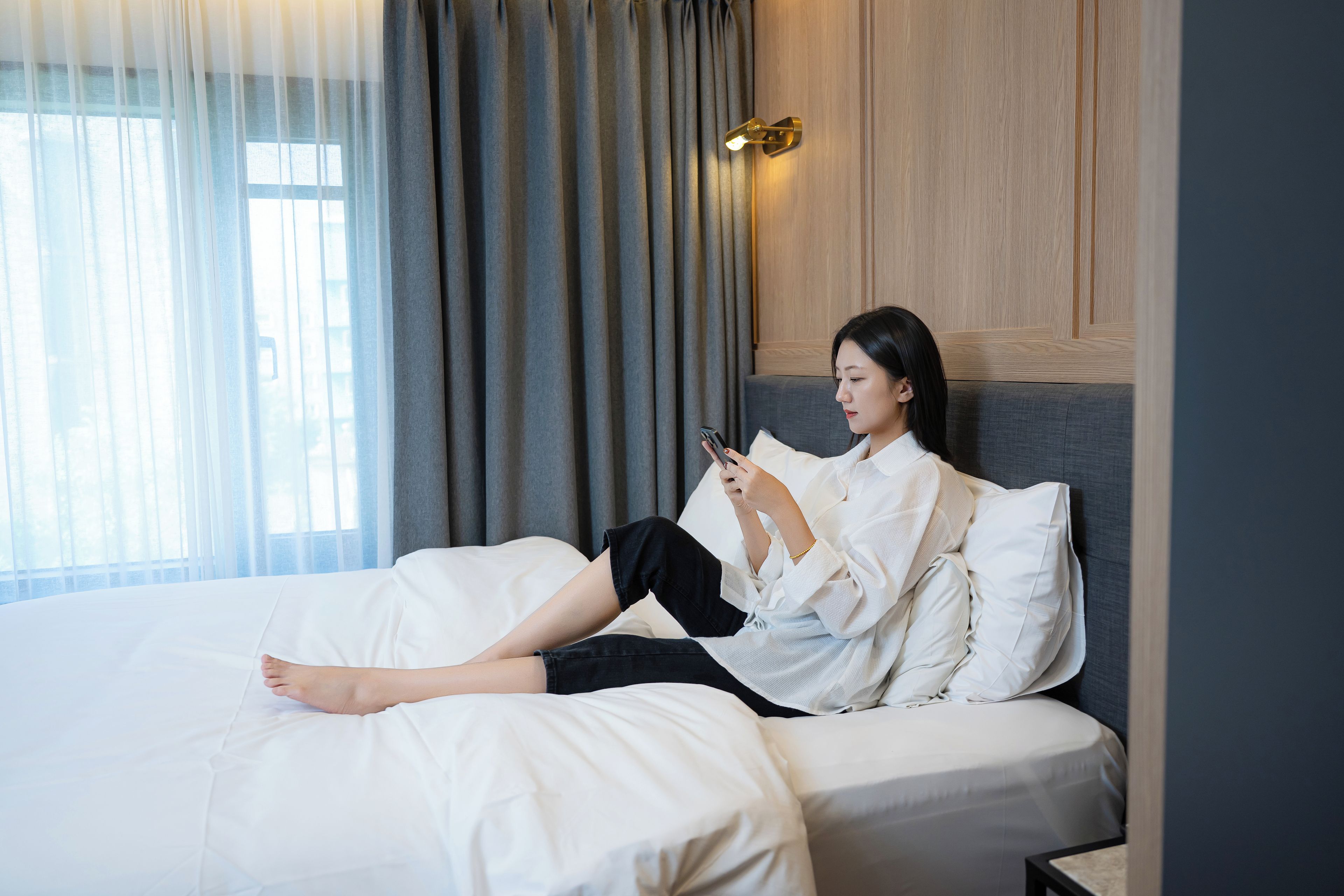 A person lying on a bed in a hotel room, reading a book.