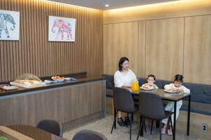 A dining area with a wooden panel wall, a reception desk with breakfast items, and two people seated at a table.