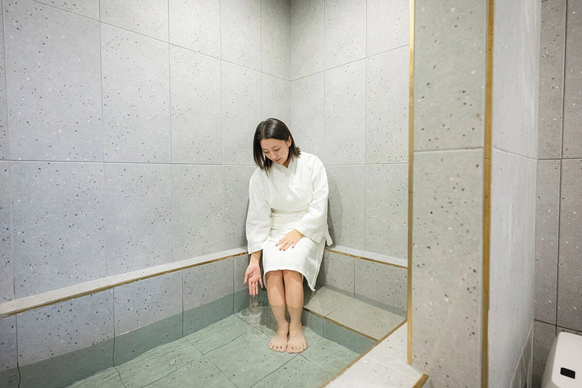 A person seated in a shower stall with a tiled floor and walls.