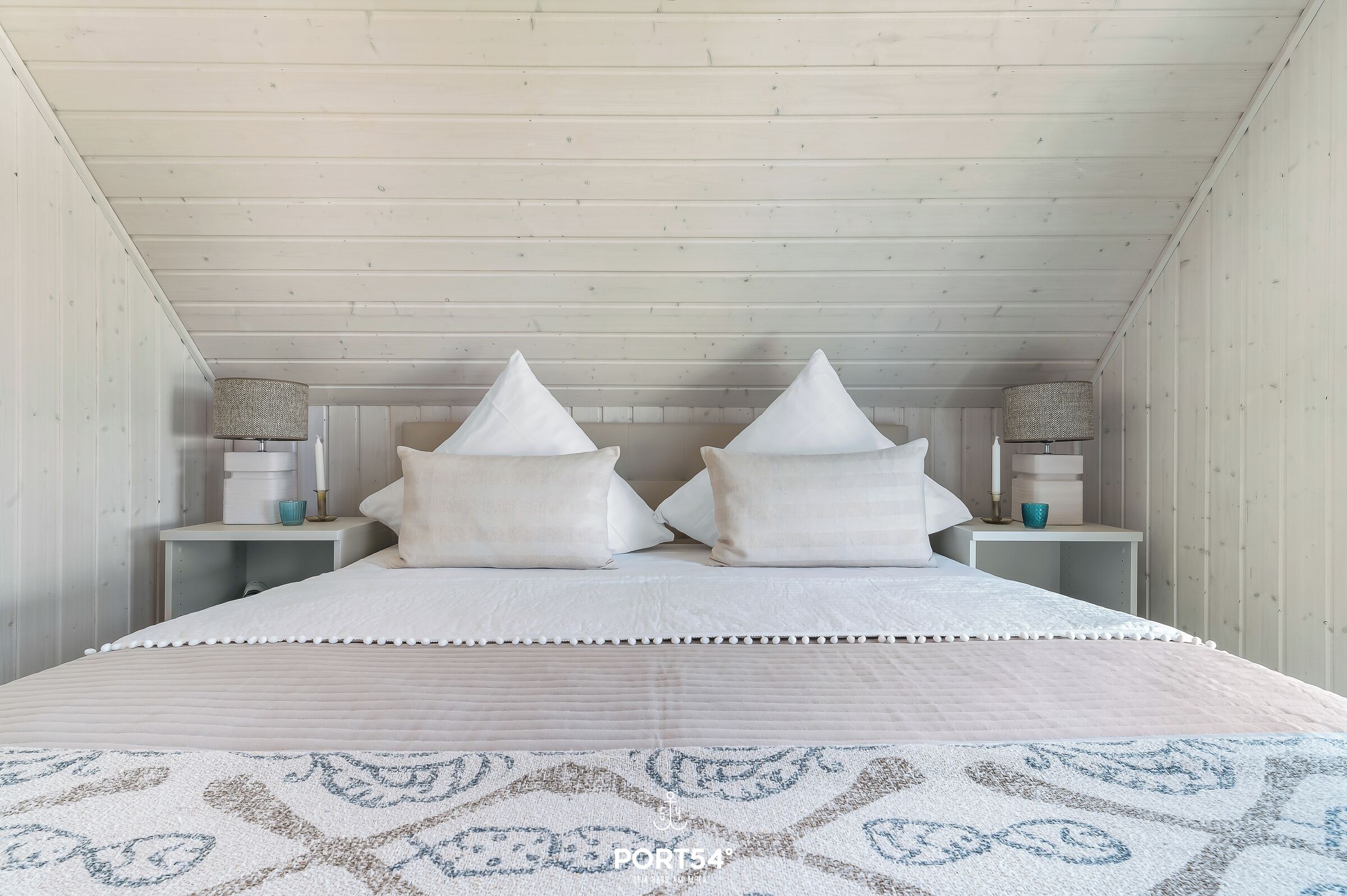 A bedroom with a bed, two nightstands, and a patterned rug.
