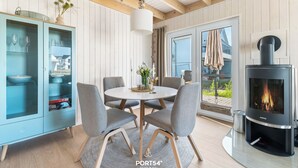 Un salon moderne avec une table ronde, des fauteuils gris, un buffet bleu aux portes vitrées, une cheminée et une vue sur l’extérieur.