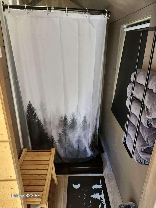 Un baño con cortina de ducha con motivos de bosque, un banco de madera y un perchero con toallas.