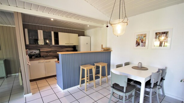 A modern kitchen with white cabinets, a blue island, and a dining area with a white table and grey chairs.