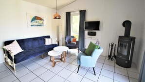 A living room with a dark blue sofa, a light blue armchair, a white coffee table, a television, and a fireplace.