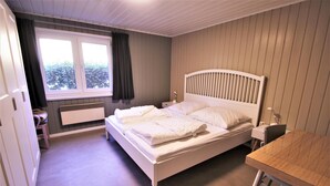 A bedroom with a bed, a desk, a chair, a radiator, and a window with curtains.