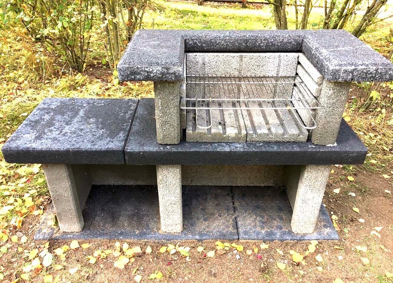 En bänk av sten med ett metallgaller i mitten, omgiven av naturlig växtlighet.