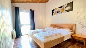 Makuuhuoneessa on puinen sänky, yöpöytä, ikkuna, jossa on verhot, ja seinälle ripustettu taulu.