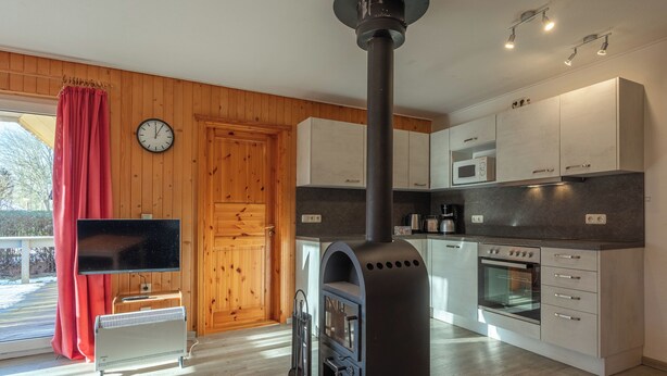 A modern kitchen with a wood stove, white cabinets, and a microwave. - Möwe 35 - Kleines Gemütliches Ferienhaus im Ferienpark Mirow (Mirow)