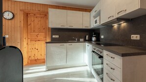 A modern kitchen with wooden paneling, a built-in oven, and a microwave. - Möwe 35 - Kleines Gemütliches Ferienhaus im Ferienpark Mirow (Mirow)