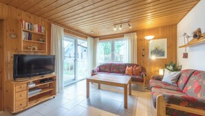A wooden-paneled living room with a flat-screen TV, a sofa, a coffee table, and a bookshelf.