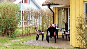 An outdoor patio with a table and chairs, surrounded by a garden and a building with a yellow facade.