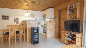 A cozy wooden interior with a dining area, a wood stove, a kitchen, and a TV.
