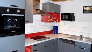 Eine moderne Küche mit grauen Schränken, einer roten Spritzschutzwand, einem eingebauten Backofen und einer Mikrowelle.