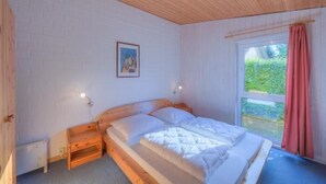 Ein Schlafzimmer mit einem hölzernen Bett, weißen Wänden, einem Fenster mit Blick auf Grünflächen und einem gerahmten Bild an der Wand.