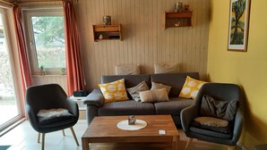 Ein Wohnzimmer mit einer Couch, zwei Sesseln, einem Couchtisch, Holzböden und einem Fenster mit Vorhängen.