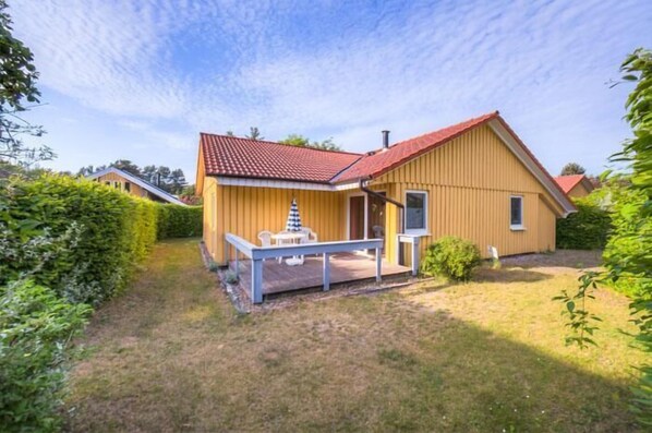 A single-story house with a red roof and yellow siding, featuring a small porch with a table and chairs.