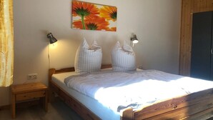 A bedroom with a wooden bed, two bedside lamps, a nightstand, and a wall-mounted painting. - Möwe 111 - Cozy vacation home in the vacation park Mirow (Mirow)
