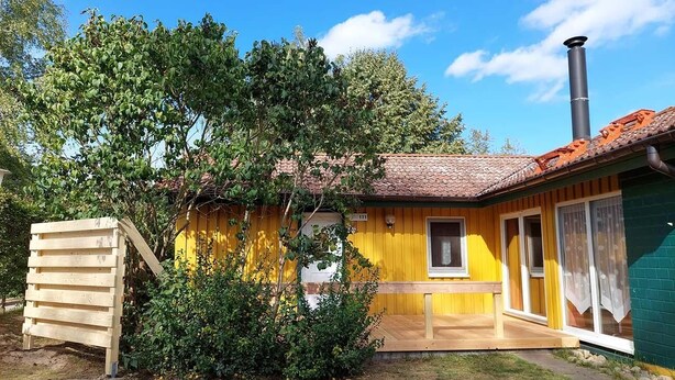 A yellow building with a tiled roof, a chimney, and a wooden structure to the left. - Möwe 111 - Cozy vacation home in the vacation park Mirow (Mirow)