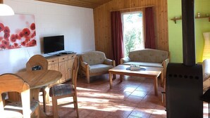 A cozy cabin interior with wooden walls, a dining area with a table and chairs, a sofa, a television, and a wood stove. - Möwe 111 - Cozy vacation home in the vacation park Mirow (Mirow)