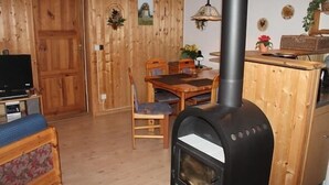 A cozy living room with a wooden interior, a dining area with a table and chairs, and a black wood-burning stove. - Möwe 151 - Kleines Gemütliches Ferienhaus im Ferienpark Mirow (Mirow)