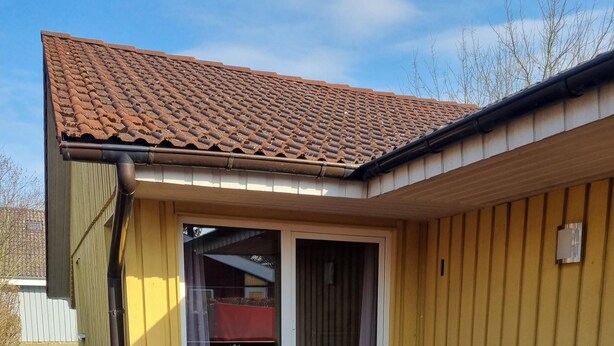 Una casa con techo de tejas, terraza de madera y puerta corrediza de vidrio.