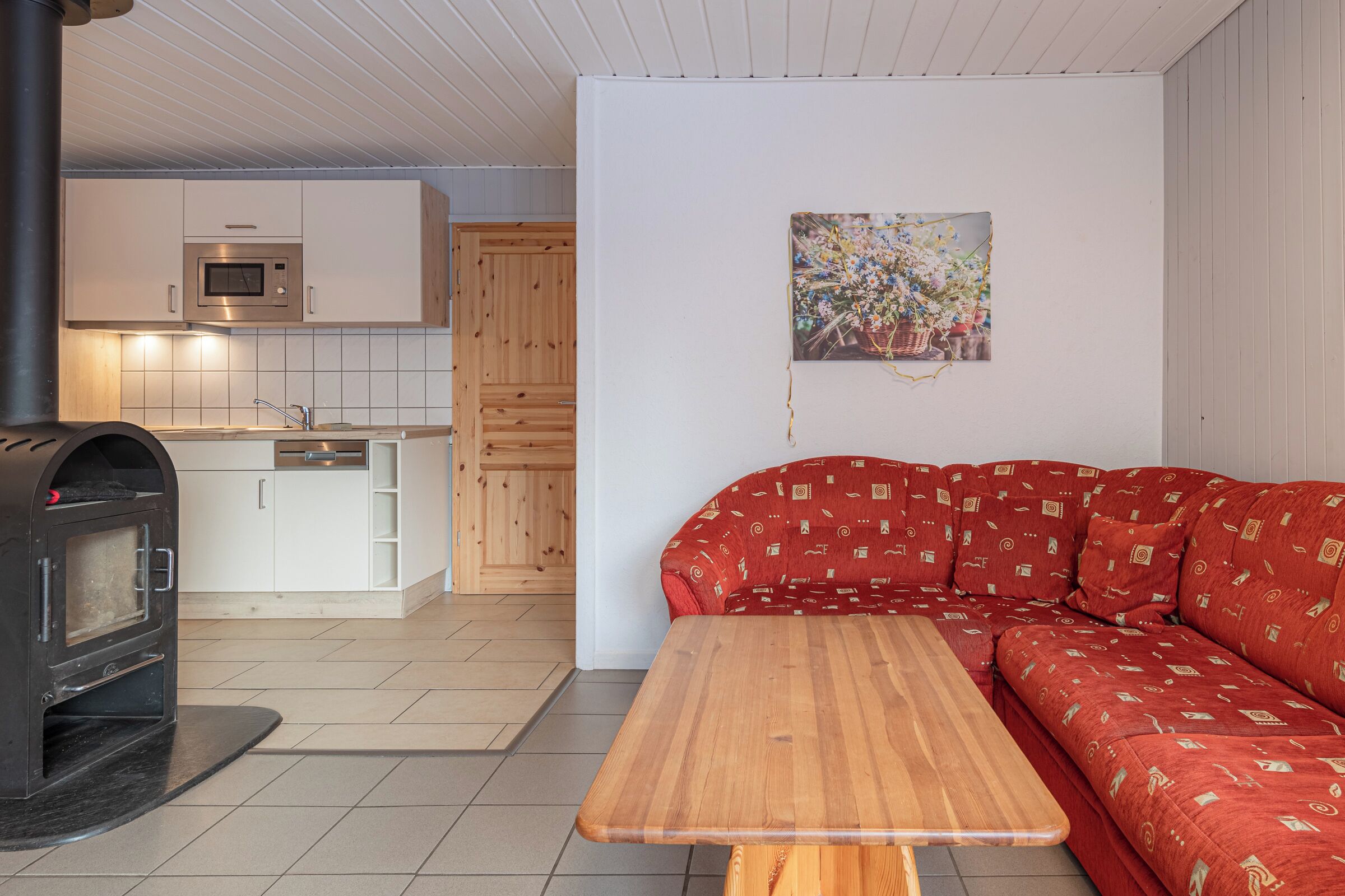 Et moderne køkken med indbygget ovn og mikroovn, en rød sofa med mønster, og et træbord.