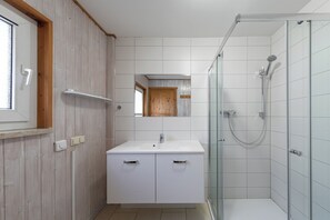 Ein modernes Badezimmer mit einem weißen Waschtisch, einer Duschkabine aus Glas und einer Holztür.