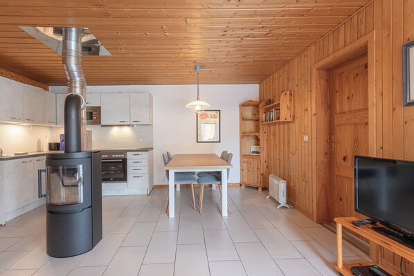 Une cuisine moderne avec un poêle à bois, des armoires blanches et un coin repas équipé d’une télévision et d’une télécommande.