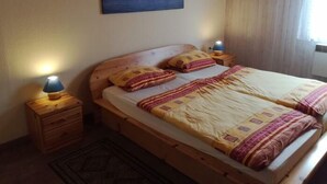 Un dormitorio con cama de madera, dos lámparas de noche, una mesita de noche, una alfombra estampada y un cuadro de paisaje urbano en la pared.