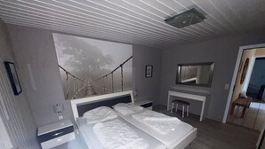 A modern bedroom with a large bed, bedside tables, a desk, a chair, and a mirror. - Milan 34 - Ferienbungalow auf Einer Ebene f ür 4 Personen (Mirow)