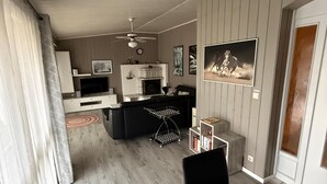 A modern kitchen with a built-in oven, a dining area with a table, and a living space with a sofa and fireplace. - Milan 34 - Ferienbungalow auf Einer Ebene für 4 Personen (Mirow)