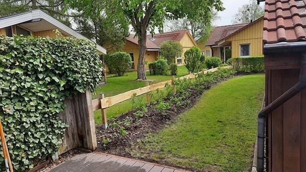 A residential area with a wooden fence, a well-maintained lawn, and houses with yellow and brown exteriors. - Milan 34 - Ferienbungalow auf Einer Ebene für 4 Personen (Mirow)