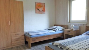 Ein Schlafzimmer mit einem hölzernen Bett, einem Nachttisch, einem Kleiderschrank, einem Fenster und einem Bild an der Wand.