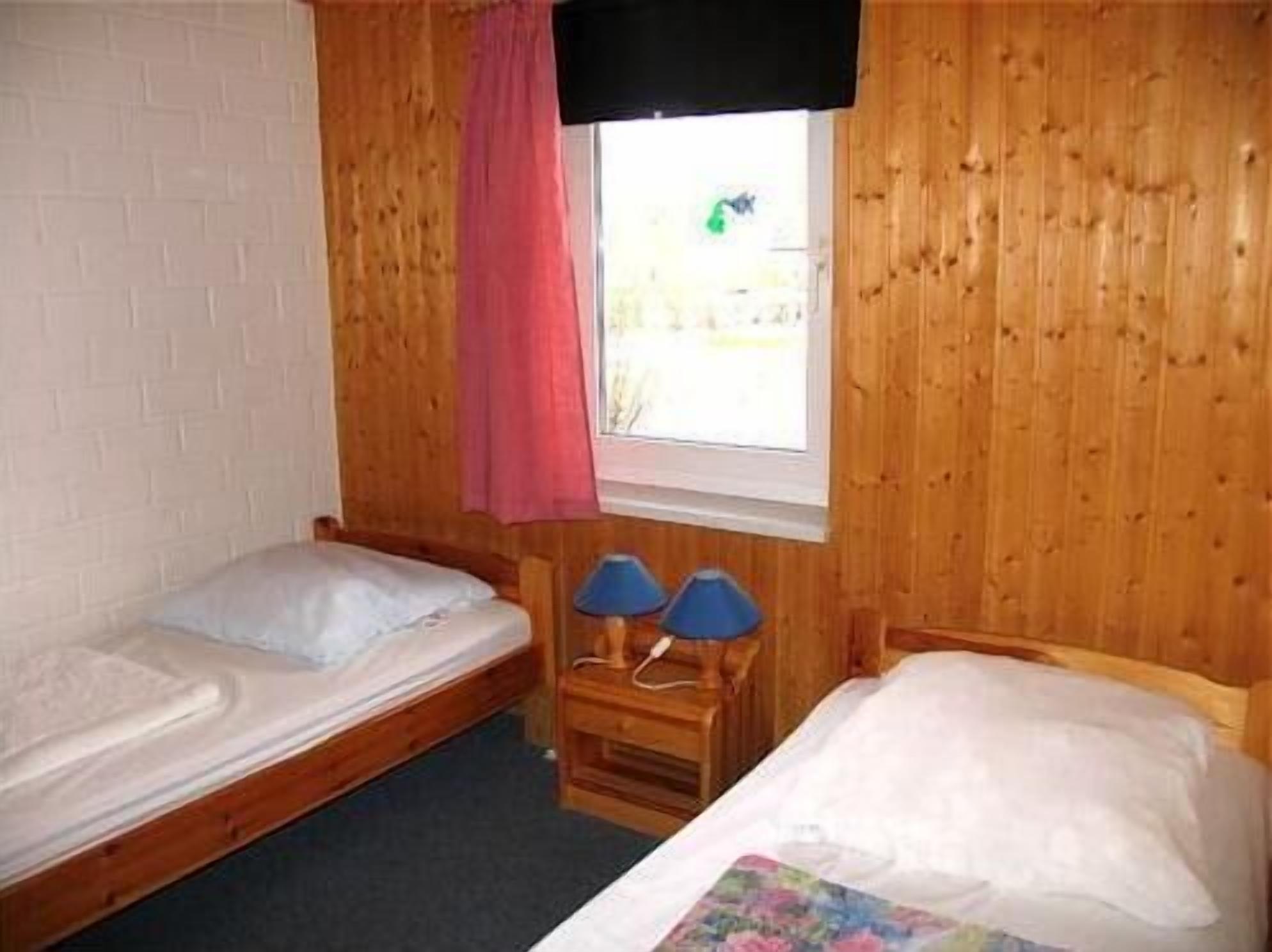 Una habitación pequeña con dos camas individuales, una ventana con cortina y una pared de madera.