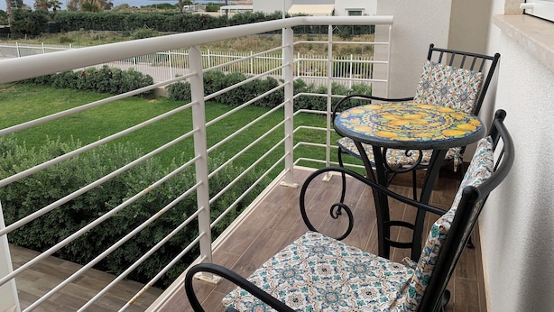 A balcony with a table and chairs, a white railing, and a view of the sea and greenery. - Villa Serendipity Terrasini (Terrasini)