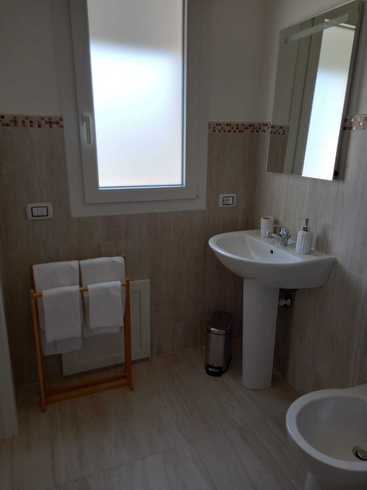 Un bagno con finestra, lavandino, specchio, porta asciugamani e bidet.