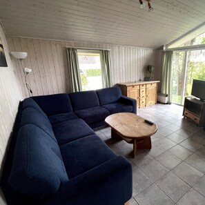 Ein Wohnzimmer mit einem blauen Sofa, einem Holztisch, einem Fernseher und einem Schrank.
