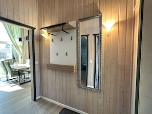 A modern interior with wooden panel walls, a large mirror, wall-mounted hooks, and a dining area with a table and chairs.