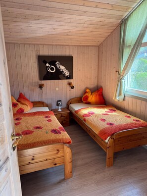 Una habitación de madera con dos camas, un cuadro en la pared, una mesita de noche y una ventana.