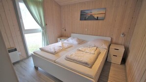 A bedroom with a large bed, a bedside table, a nightstand, and a window with curtains.