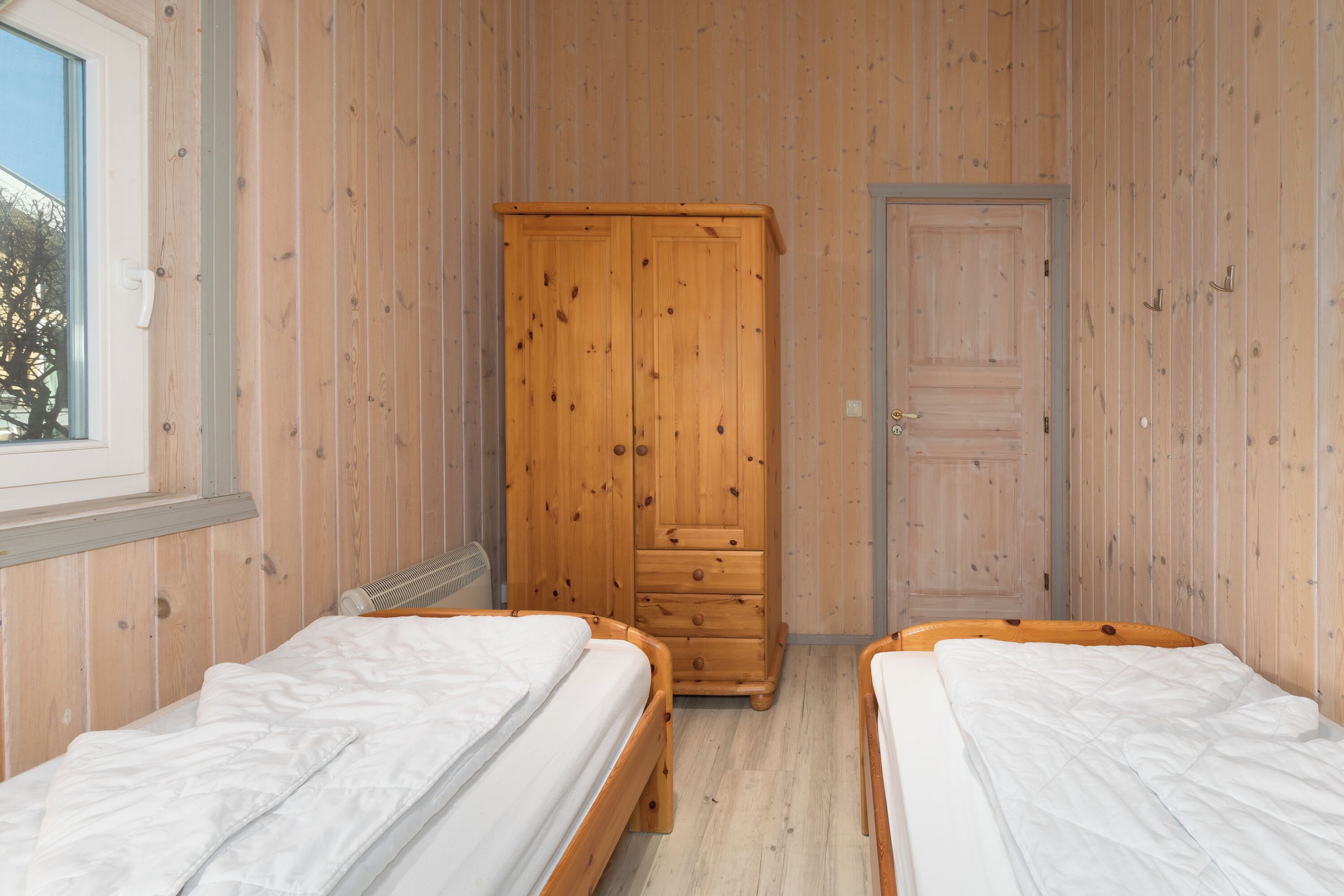 Una habitación con dos camas de madera, un armario de madera y una puerta.