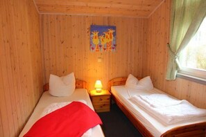 Et lille, hyggeligt rum med trævægge og to senge. Et natbord med lampe står mellem sengene.
